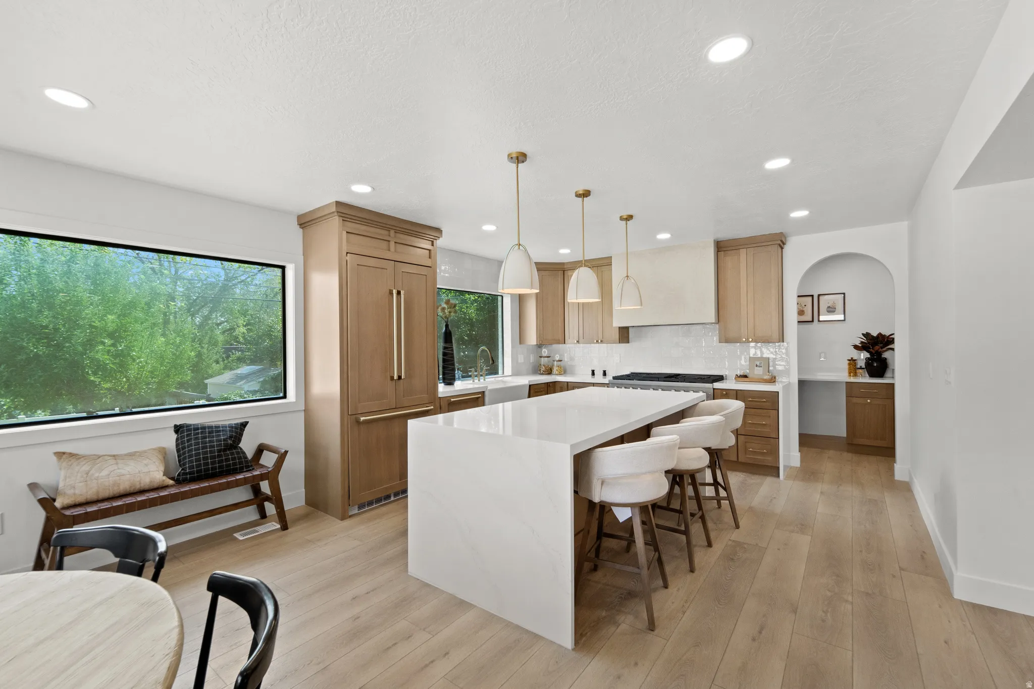 Bright kitchen featuring wood-finish flooring, a large island with a light-toned countertop, recessed lighting, and integrated panel-ready appliances