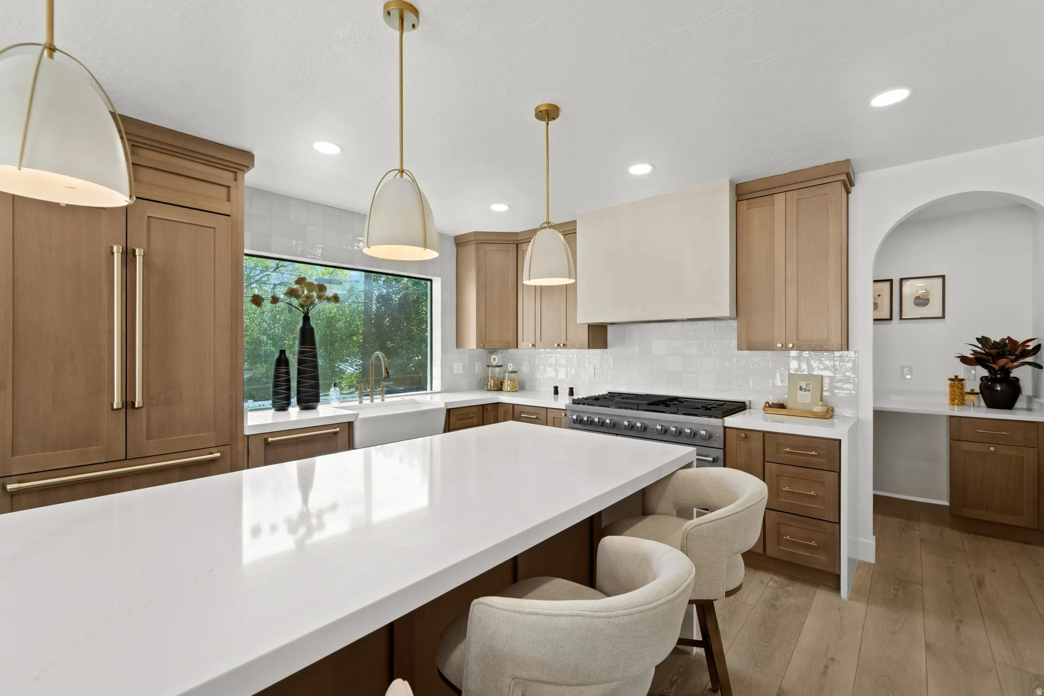 Spacious kitchen featuring a large central island with a white countertop, built-in panel-ready refrigerator, stainless steel range with custom vent hood, and natural wood-finish cabinetry