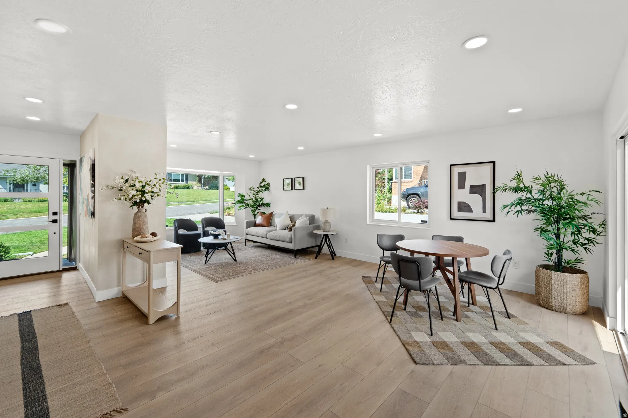 Expansive open-concept living area featuring wood-finish flooring, recessed lighting, large windows, and a glass-paneled entry door