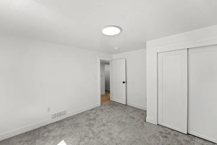 Light gray carpet, white walls, flush-mount ceiling light, white sliding closet doors, and a white interior door with black hardware