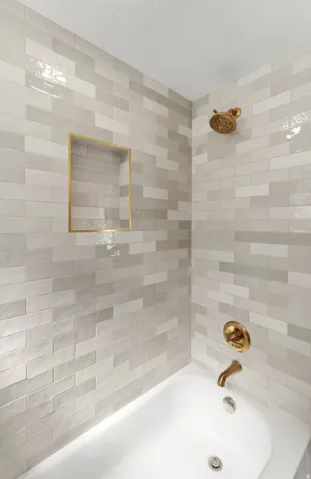 White porcelain bathtub with a built-in niche, gold-finish fixtures, and subway-style tile surround