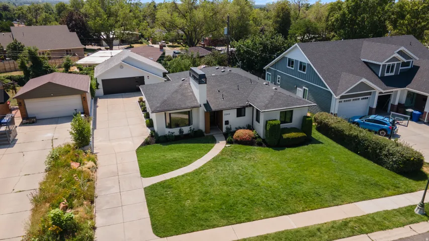 White stucco exterior with dark trim windows, front yard with manicured lawn, curved concrete walkway, and mature landscaping