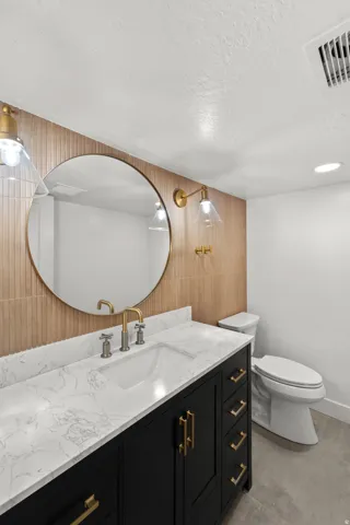 Black vanity with gold hardware, white countertop with integrated sink, gold-toned wall sconces, and a round wall mirror