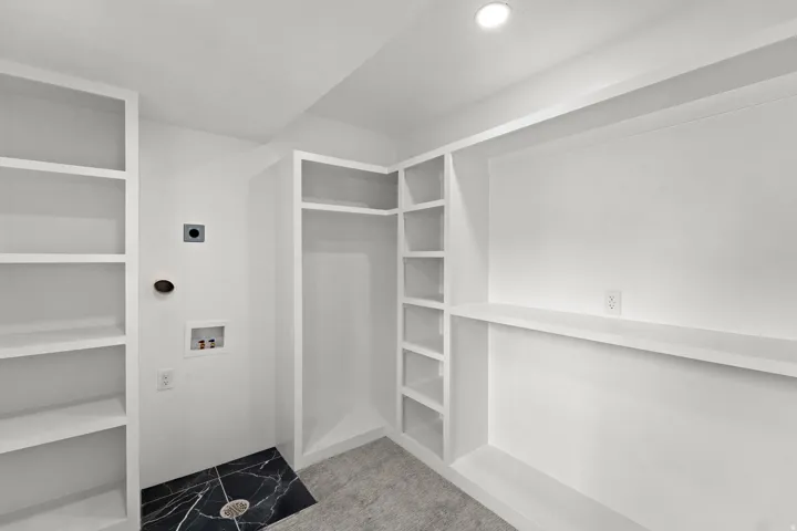 Built-in shelving, integrated closet space, recessed lighting, and a dark stone-finish floor section with drainage
