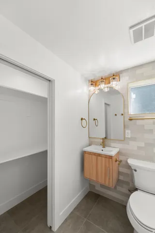 Floating wood-finish vanity with an integrated sink, gold-toned fixtures, and a tiled accent wall