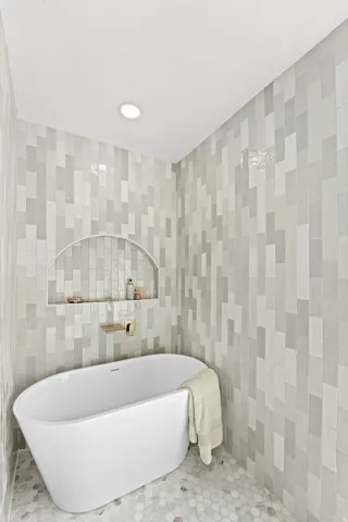 Freestanding bathtub with an arched wall niche, gold-finish fixtures, and mosaic hexagon floor tiles