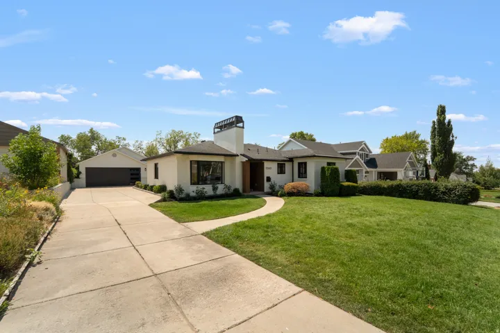 White stucco exterior with dark trim windows, an attached two-car garage, an elongated concrete driveway, a curved pathway, and a front lawn