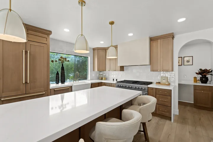 Spacious kitchen featuring a large central island with a white countertop, built-in panel-ready refrigerator, stainless steel range with custom vent hood, and natural wood-finish cabinetry