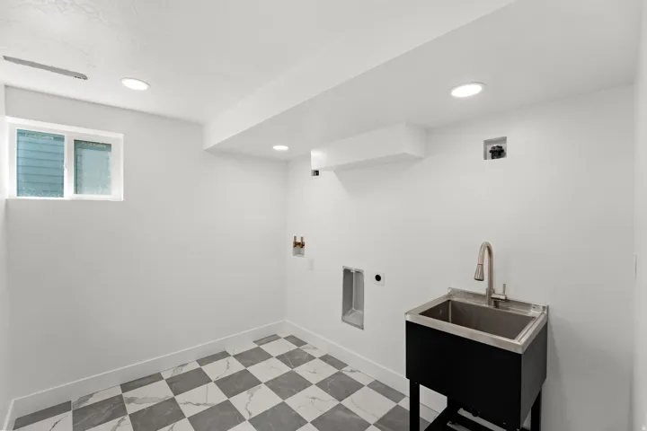 Utility sink with stainless steel basin, checkered tile flooring, recessed lighting, and a window