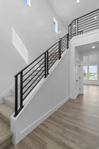 Open-concept entry with wood-finish flooring, a carpeted staircase, and a modern black metal railing
