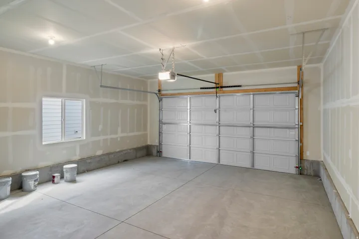 Spacious garage featuring a concrete floor, a white paneled garage door, a window with horizontal blinds, and a garage door opener