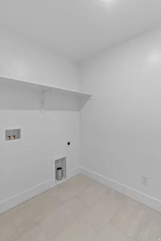 Laundry space with light-toned rectangular floor tiles and a white wall shelf
