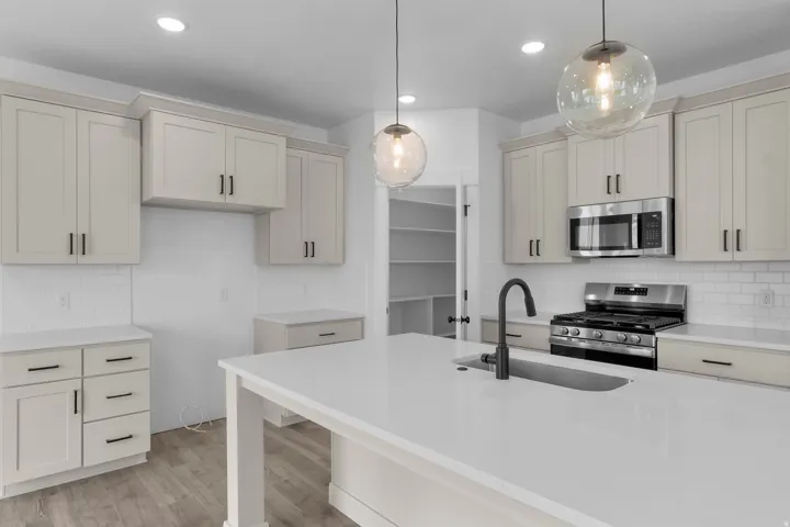 Kitchen featuring a center island with sink, stainless steel appliances, neutral cabinetry, and wood-finish flooring