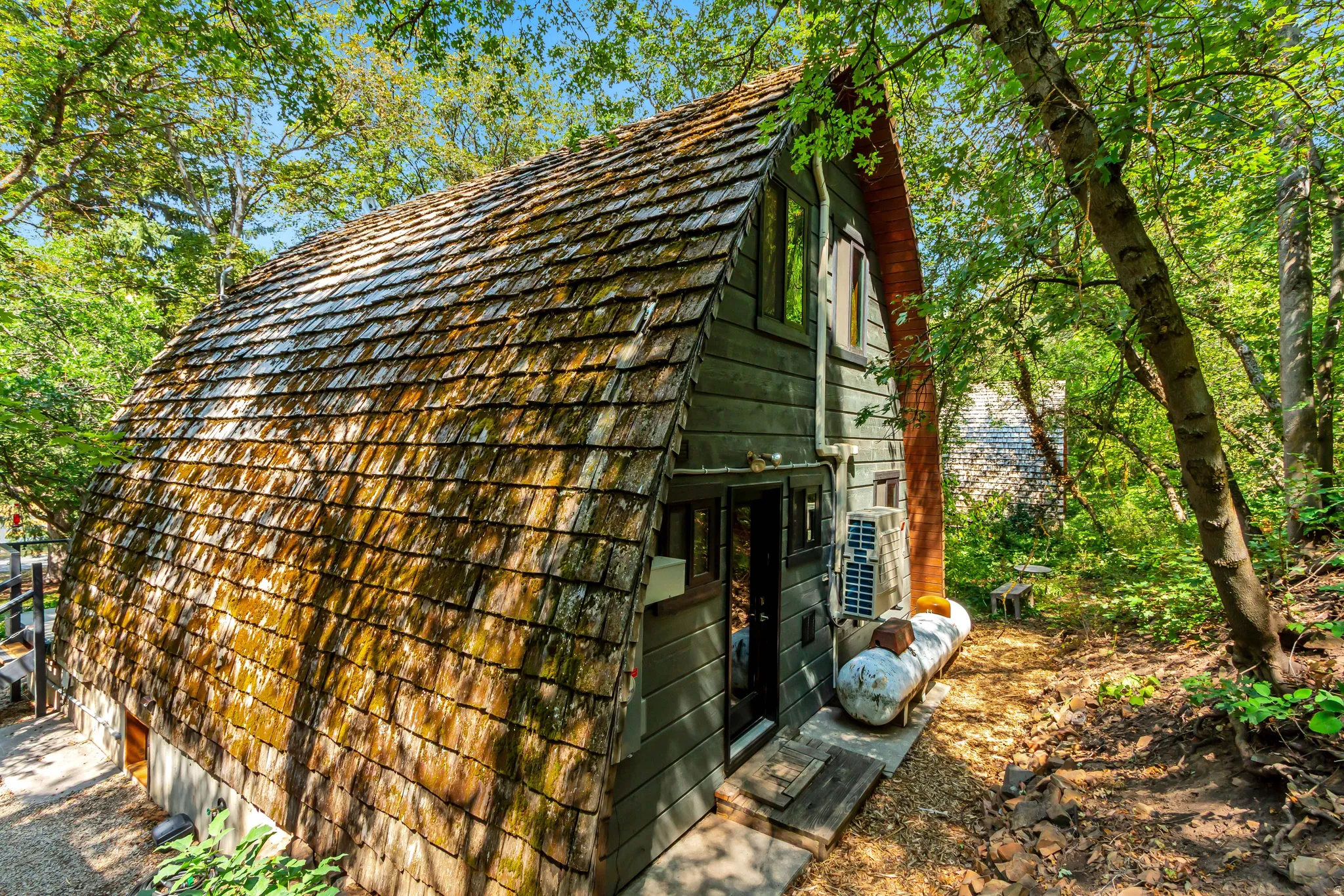 Back of home showing mini-split heating and cooling and propane tanks