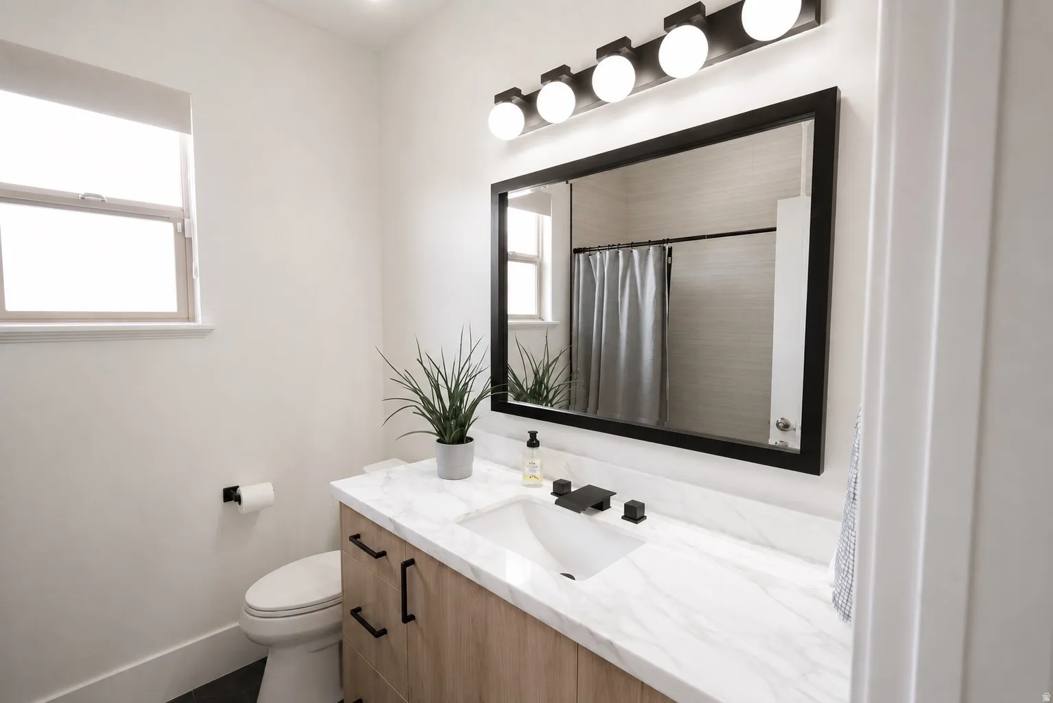 Bathroom featuring a single window, a wood-finish vanity with drawer pulls, a countertop with an integrated sink, a wall-mounted mirror, and a wall-mounted light fixture
