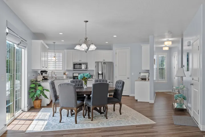 Open-concept living space with wood-finish flooring, white cabinetry, stainless steel appliances, and a glass sliding door