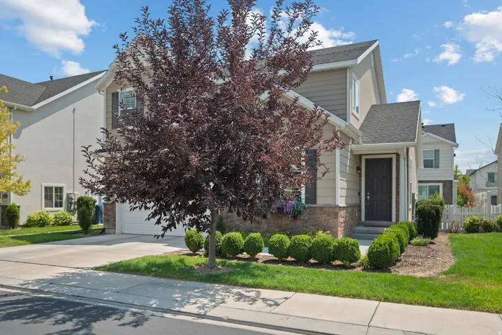 Siding exterior with stone veneer accents, attached garage, covered entryway, and mature landscaping