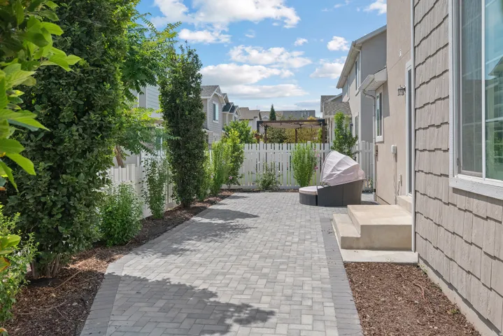 Paved patio area, white picket fence, mature landscaping, shingle siding, and stucco exterior