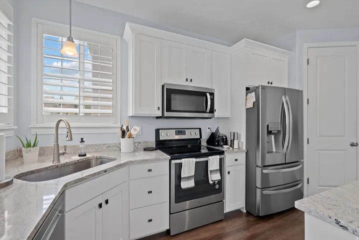 White cabinetry with dark hardware, stainless steel appliances, light-toned countertops, undermount sink, and wood-finish flooring