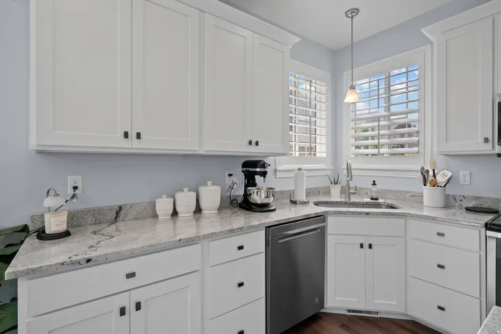White shaker cabinetry with dark pulls, light-toned stone countertops, and a stainless steel dishwasher