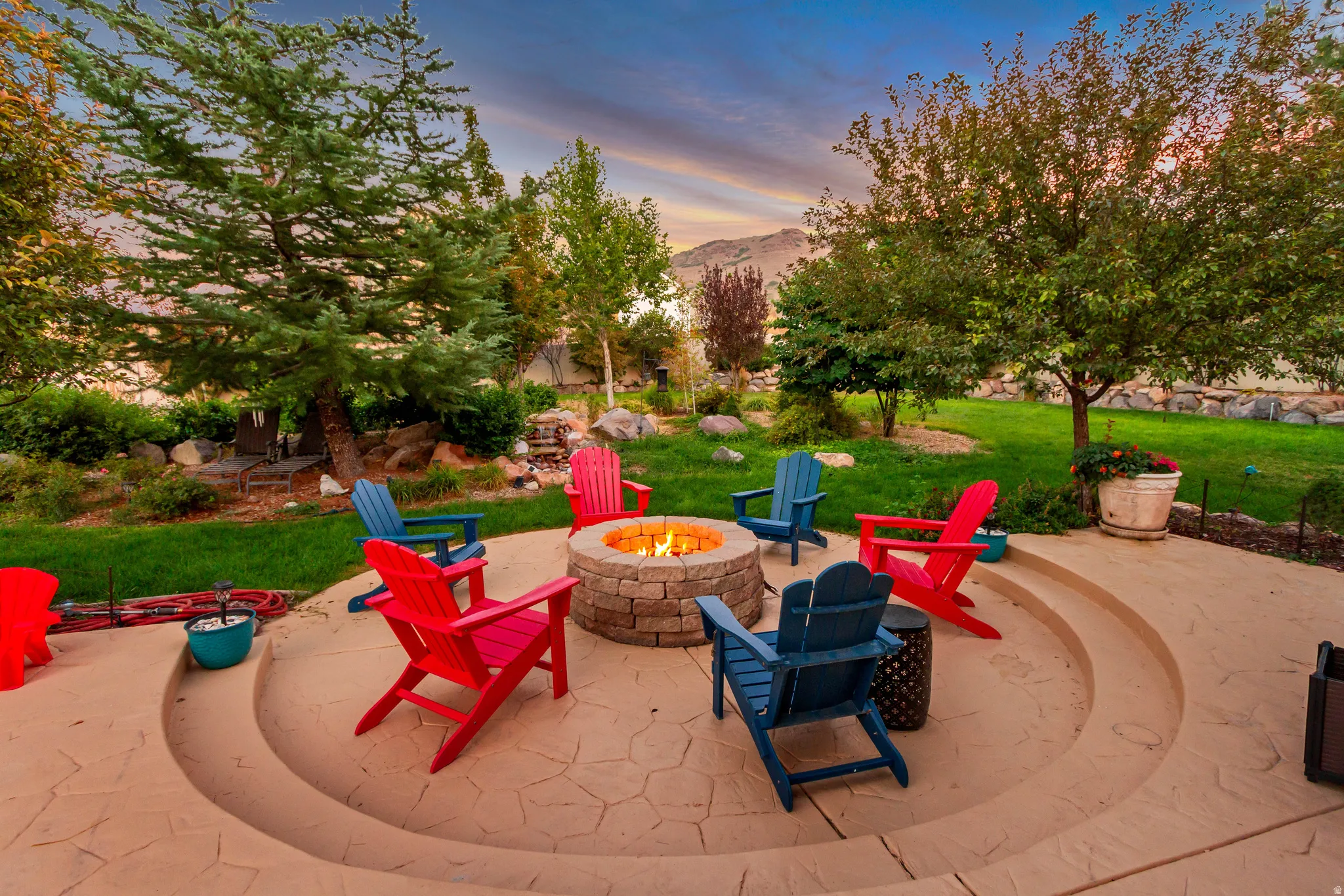 Expansive patio featuring a stone-clad fire pit, stamped concrete, and integrated seating steps