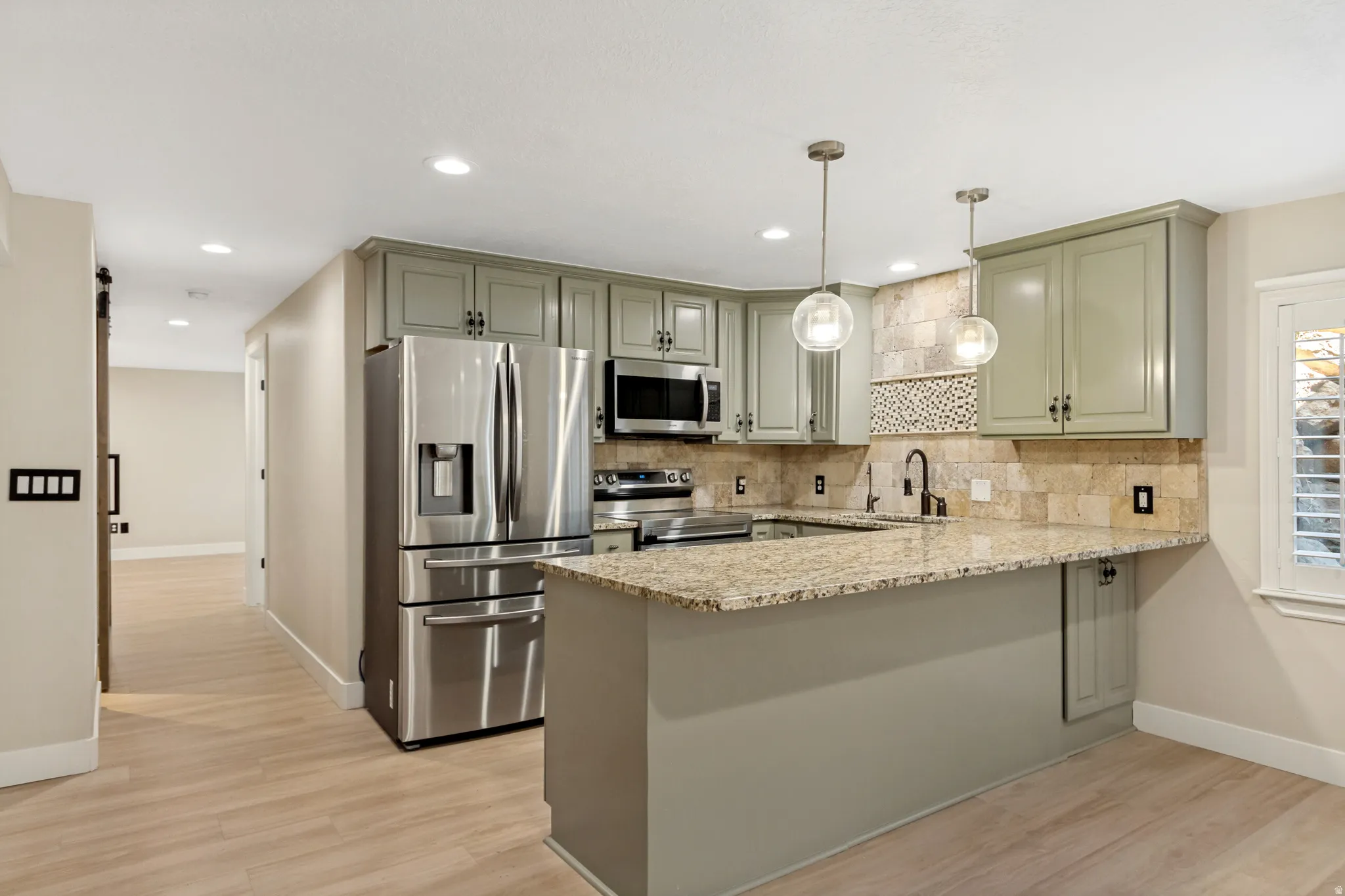 Kitchen featuring stainless steel appliances, granite countertops, light green cabinetry, and pendant lighting