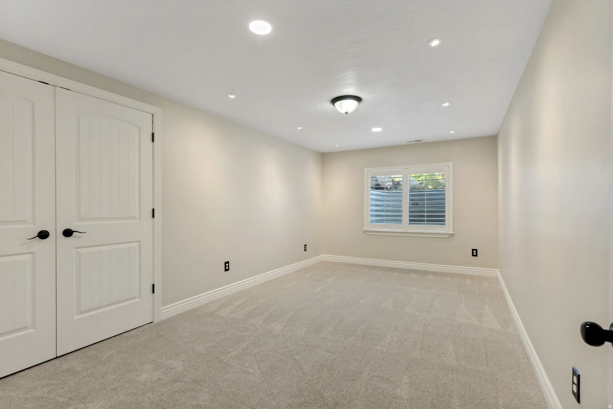 Recessed lighting, neutral wall tones, window with white blinds, light-toned carpeting, and panel doors