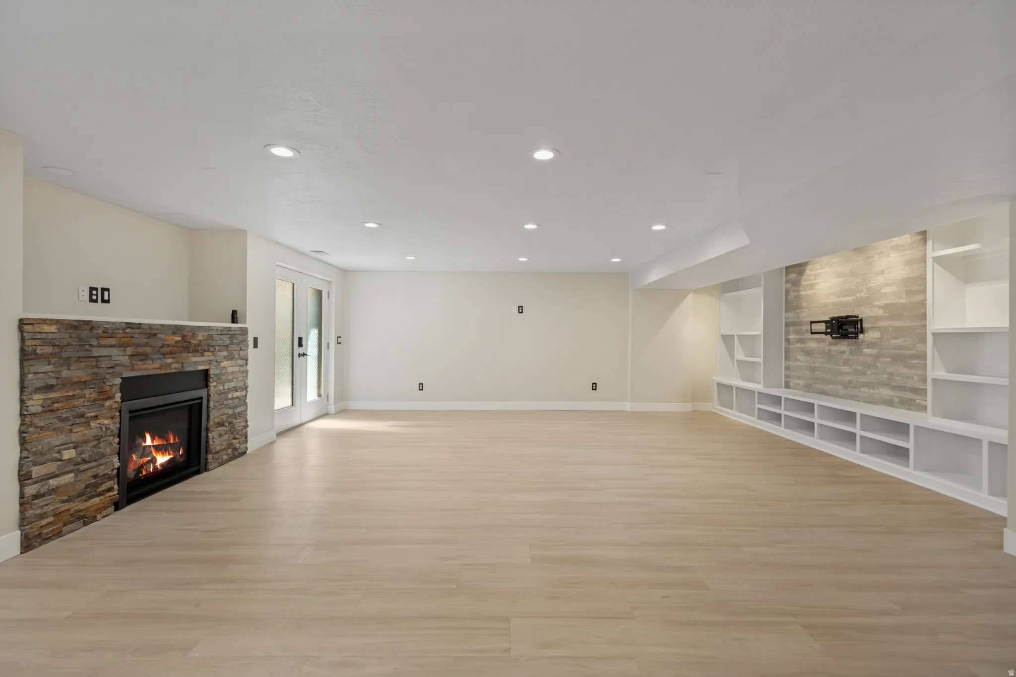 Recessed lighting, wood-finish flooring, stone-clad fireplace, integrated shelving, and French doors