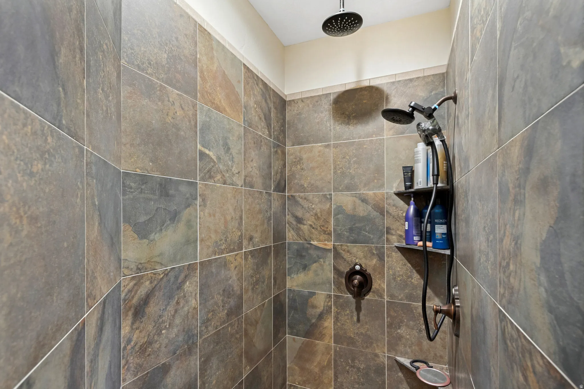 Shower with multi-toned tile walls, a rain shower head, and an additional shower head with hose attachment
