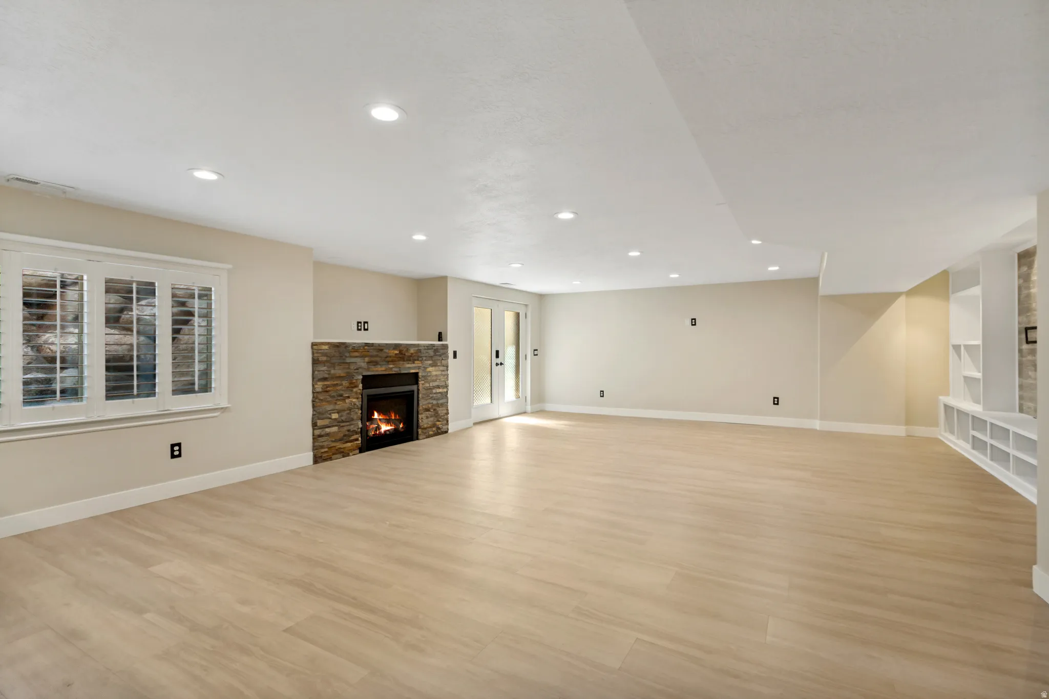 Spacious room featuring wood-finish flooring, a stone-clad fireplace, recessed lighting, and built-in shelving