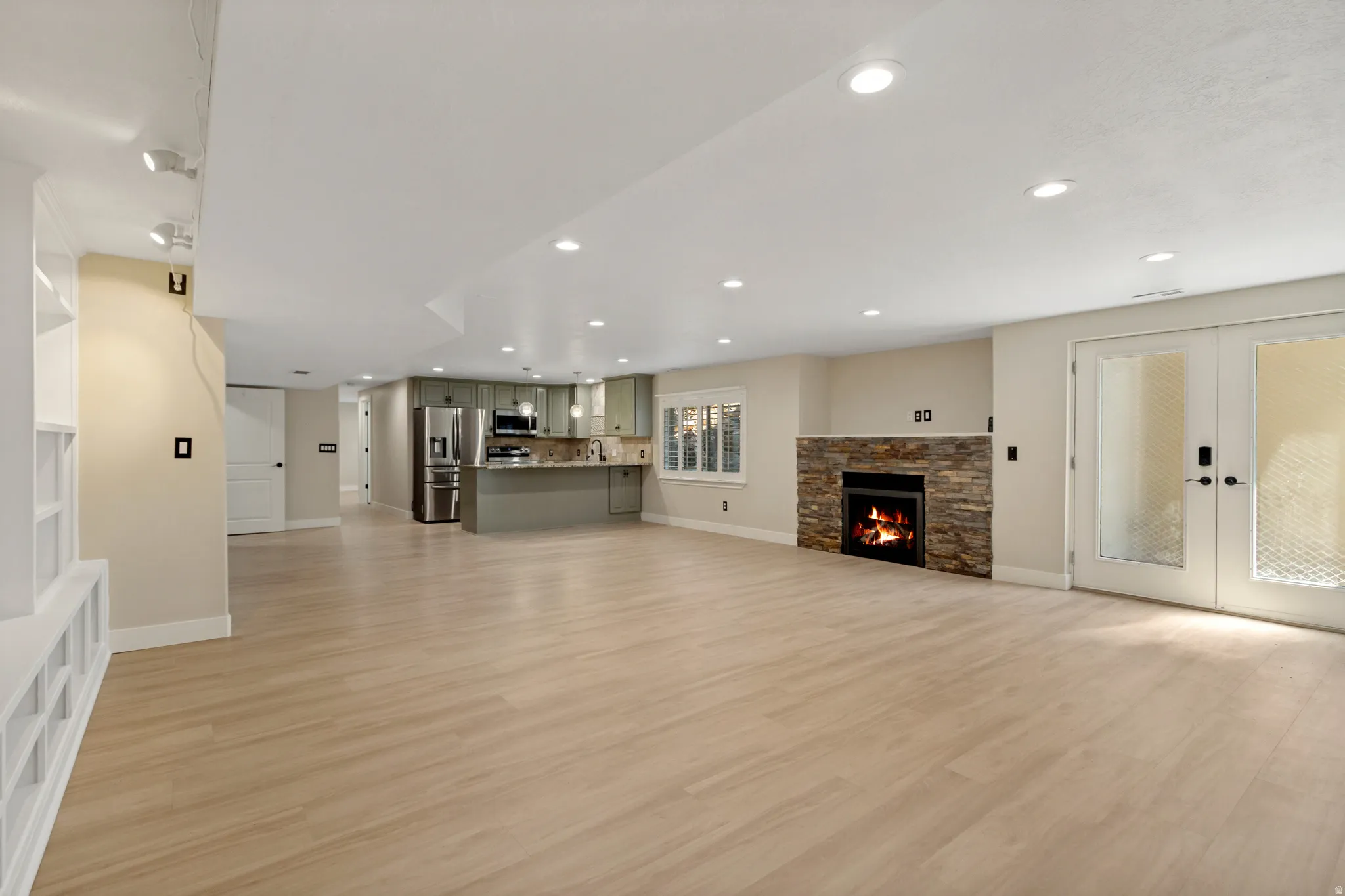Expansive open-concept room with wood-finish flooring, recessed lighting, and a stone-clad fireplace