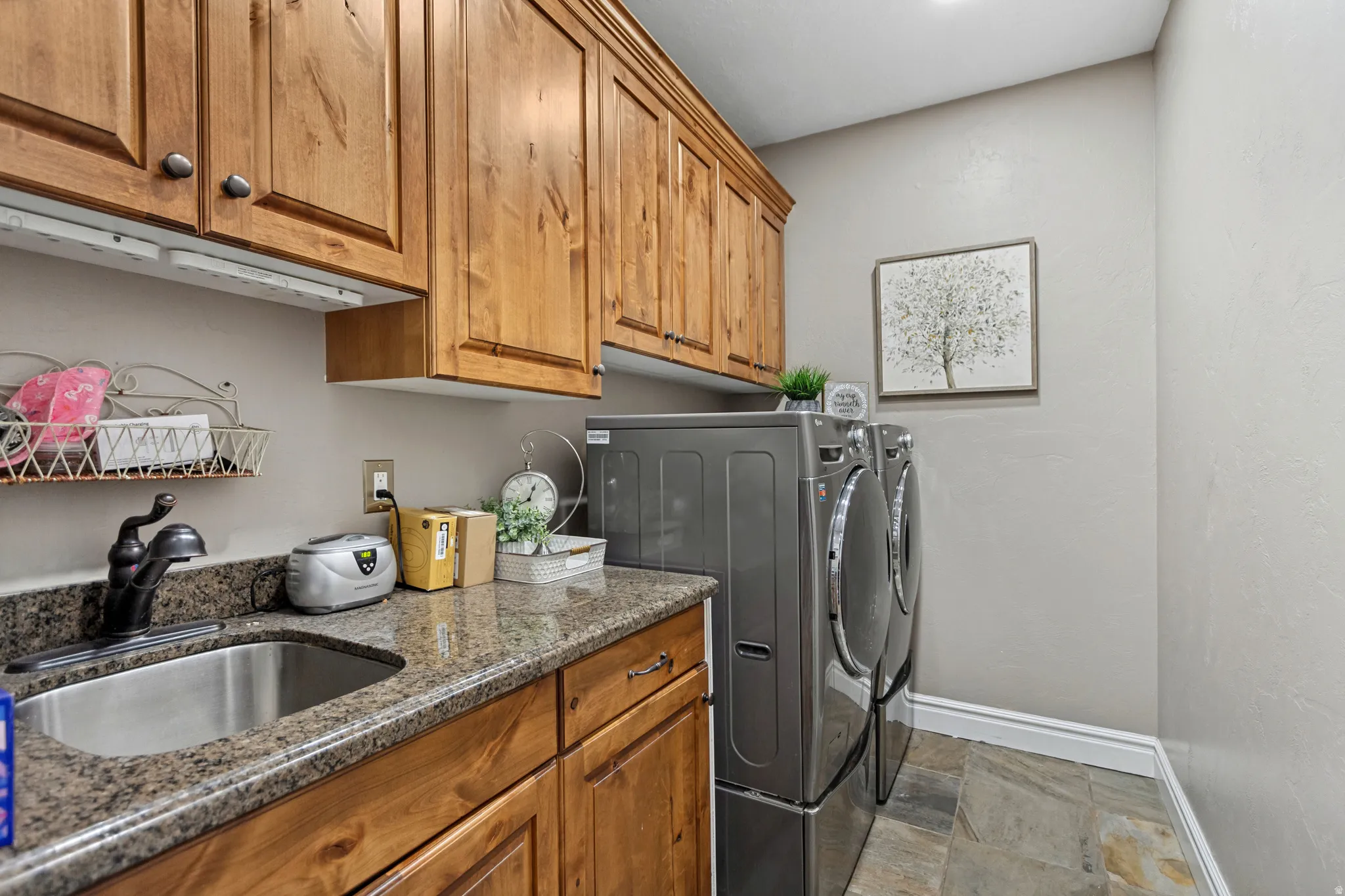 Laundry area featuring natural wood cabinetry, granite-style countertop, stainless steel sink, and slate-style flooring