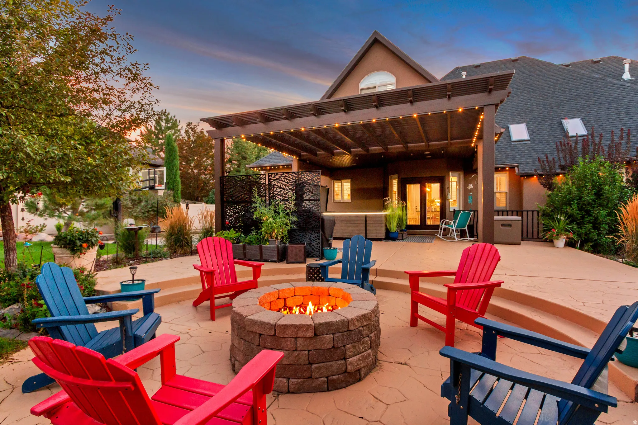 Expansive patio featuring a stone-finish fire pit, multi-level concrete pavers, and a built-in pergola with string lights