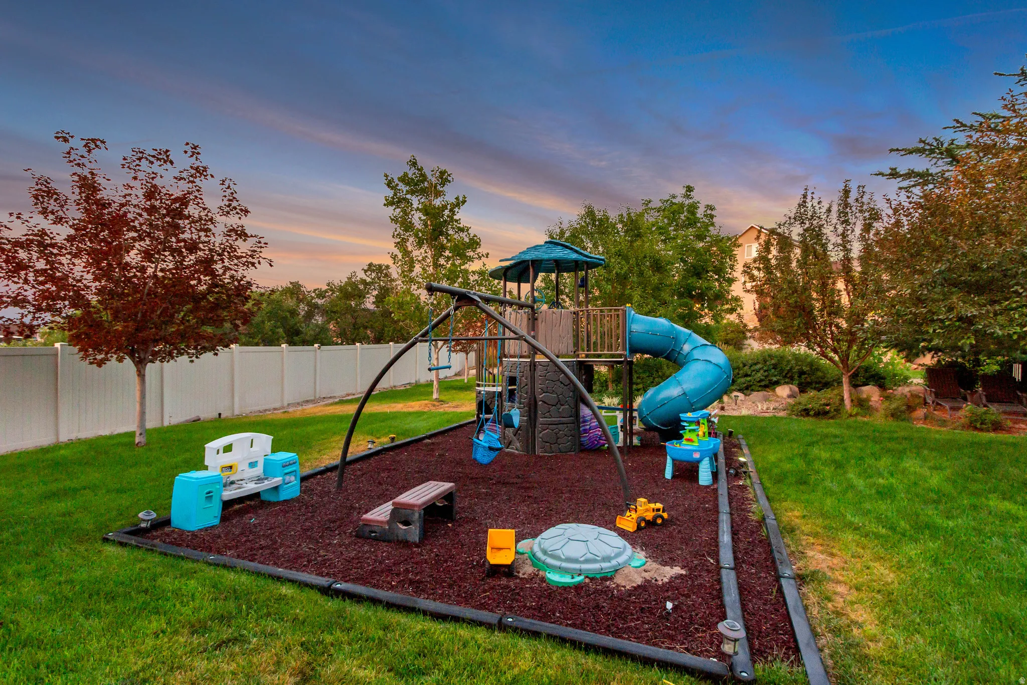 Expansive backyard featuring a manicured lawn, a white privacy fence, and mature trees