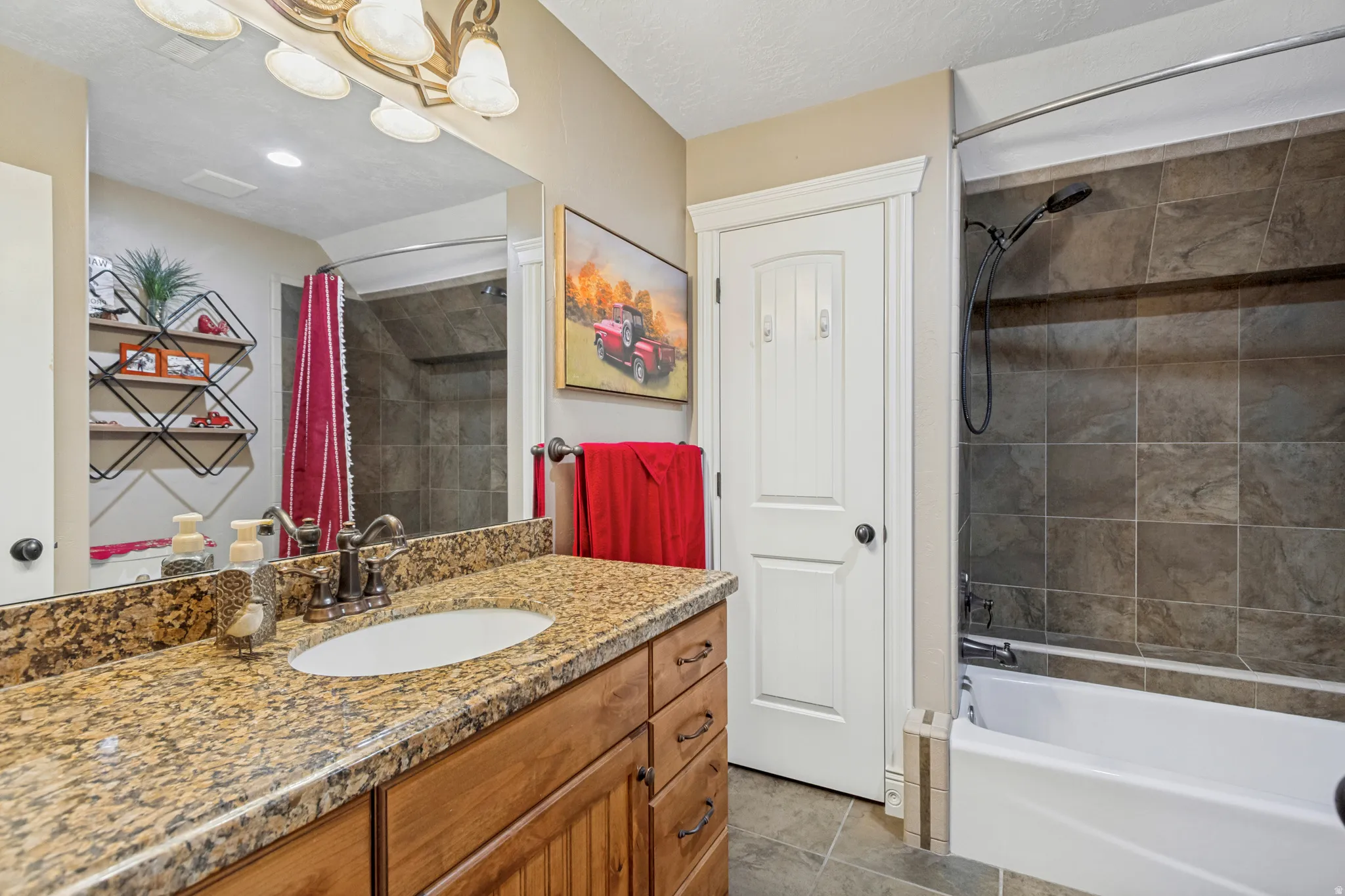 Granite-finish countertop with an undermount sink, wood-finish vanity cabinetry, and a shower-over-tub with dark tile surround