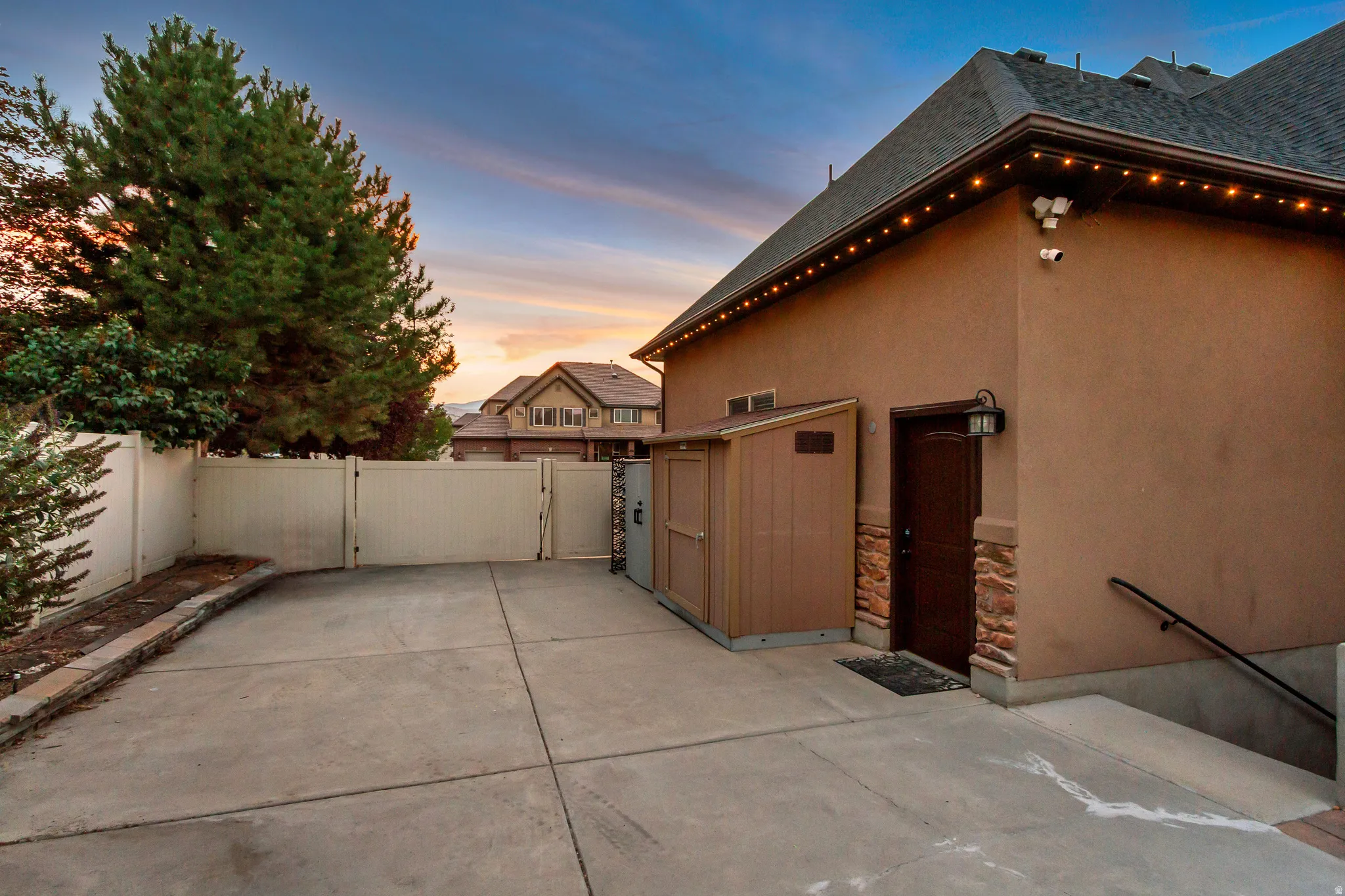 Concrete driveway, solid privacy fence, side entry door with stone surround, exterior wall sconce, and built-in storage shed