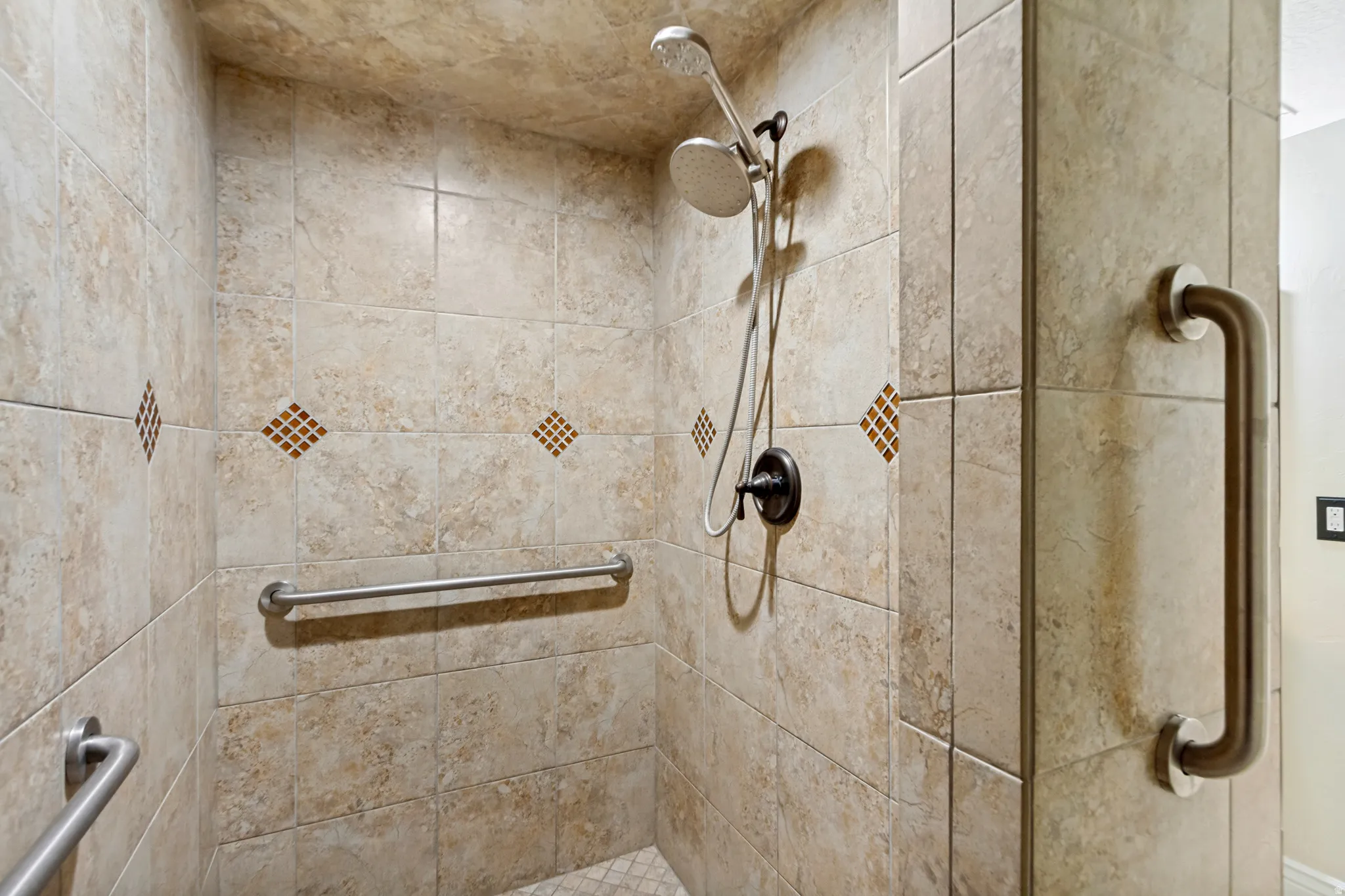 Tiled shower with decorative accent tiles, dual shower heads, and multiple grab bars