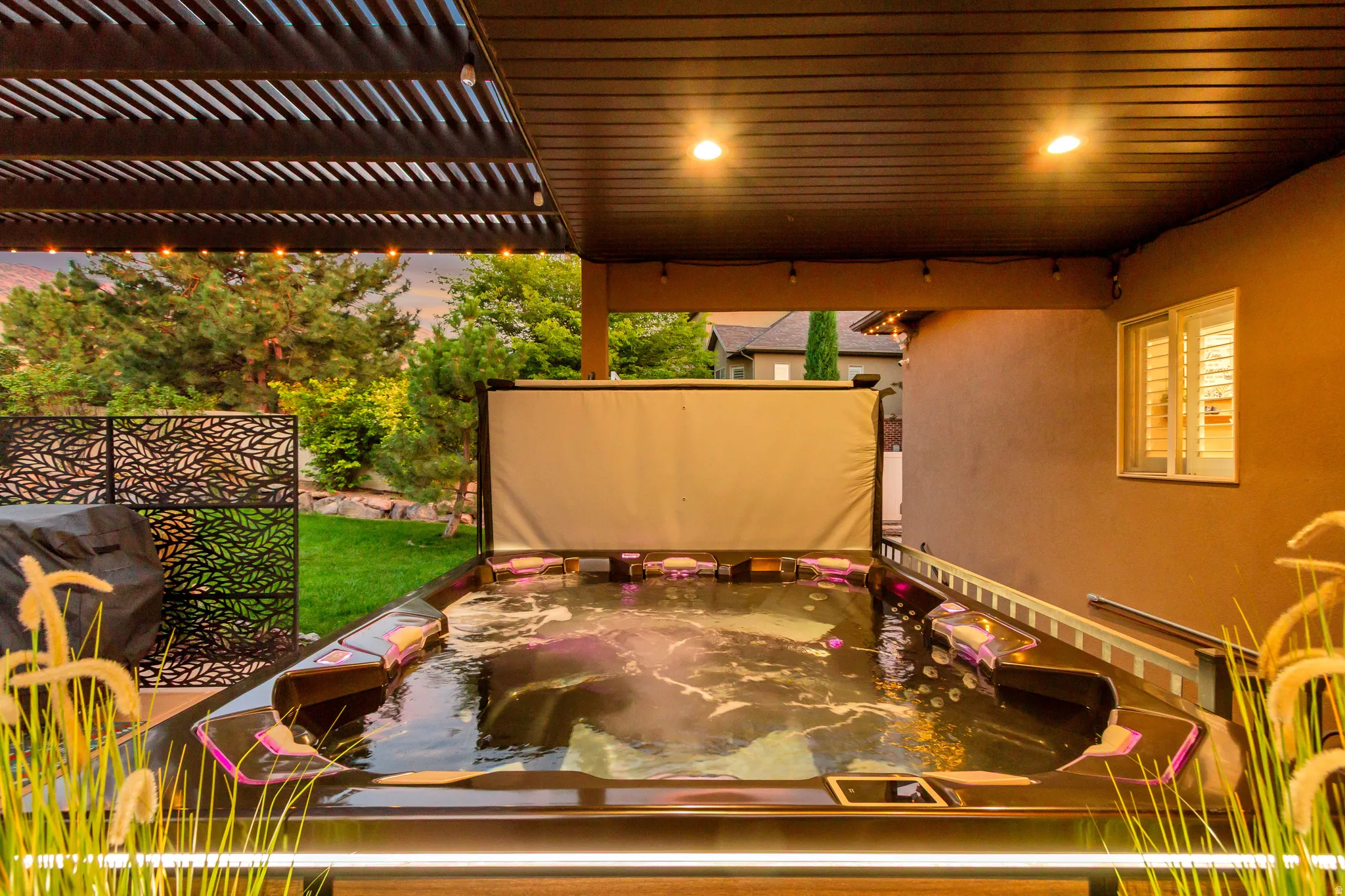 Covered patio featuring a built-in spa, slatted pergola, recessed lighting, and decorative metal privacy screens