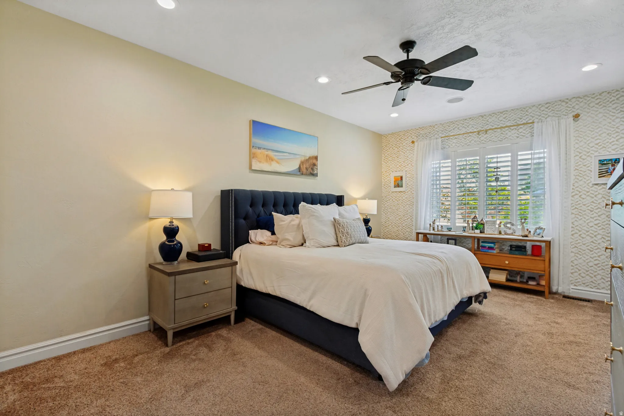 Recessed lighting, ceiling fan, plush carpet, window with plantation shutters, and a tufted headboard
