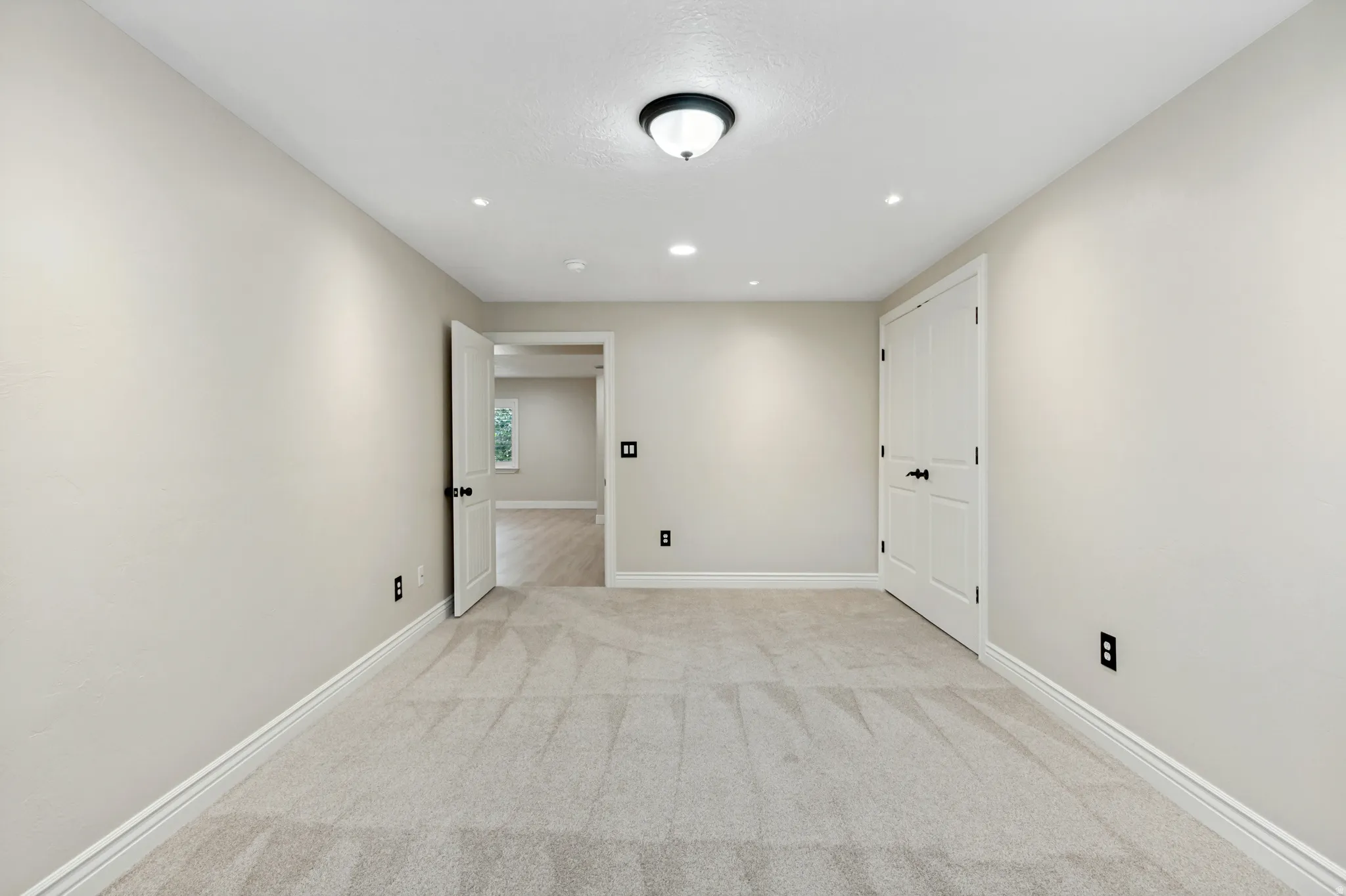 Light neutral wall paint, recessed ceiling lighting, light-toned carpet, white trim, and a white paneled door with black hardware