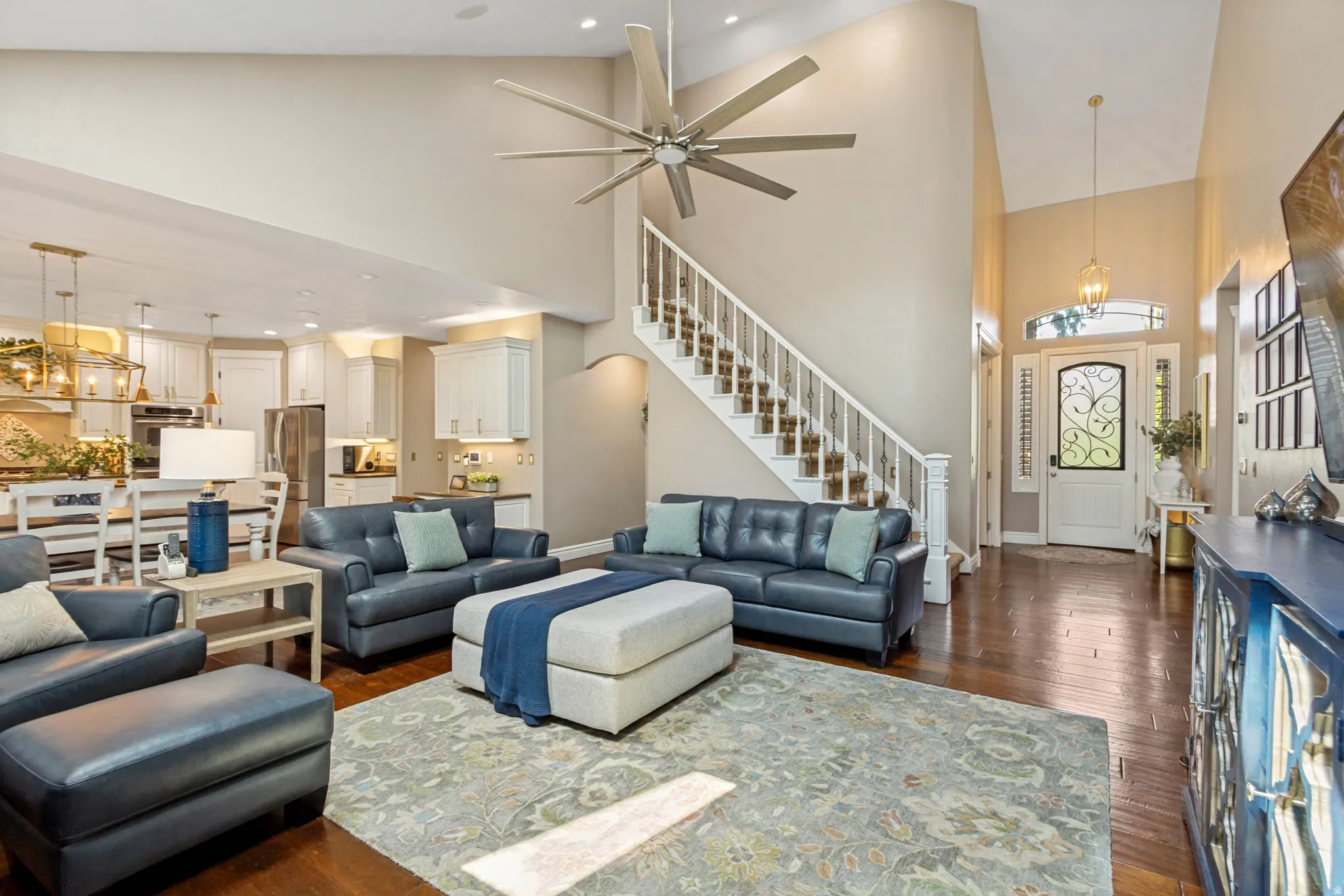 Open-concept living area with soaring ceilings, wood-finish flooring, a grand staircase, and a decorative front entry door