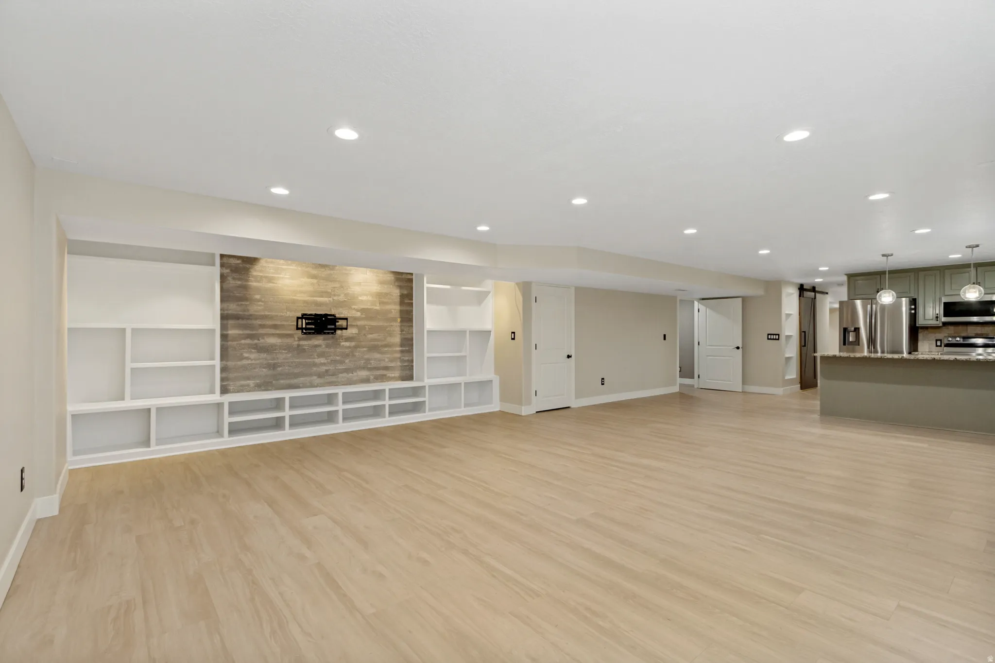 Spacious living area featuring wood-finish flooring, recessed lighting, and a built-in entertainment center with a stone-clad accent wall