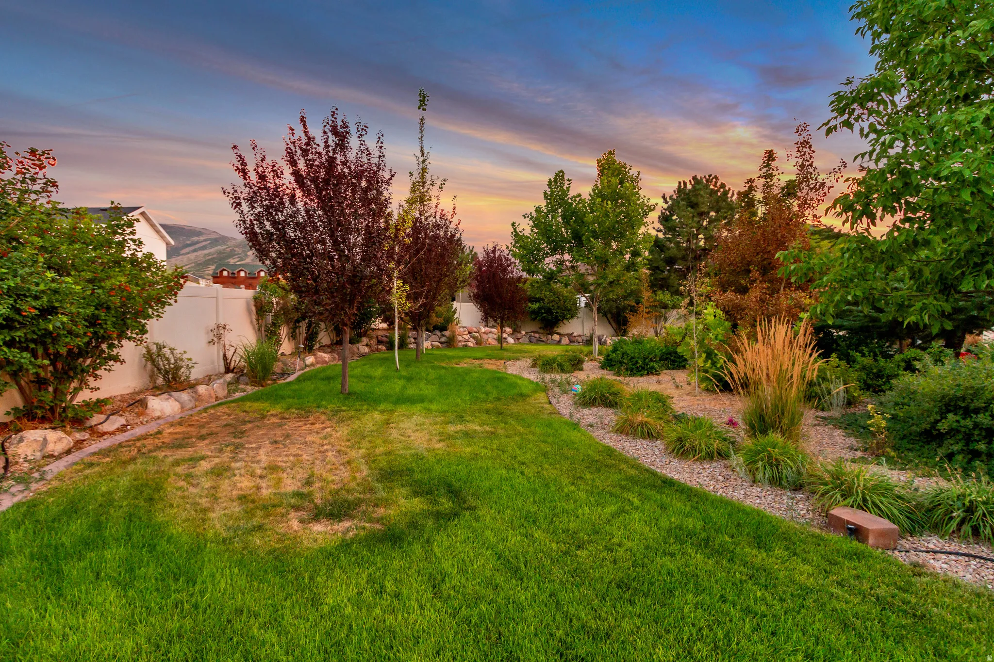 Expansive lawn area, mature trees, landscaped rock beds, and a perimeter fence