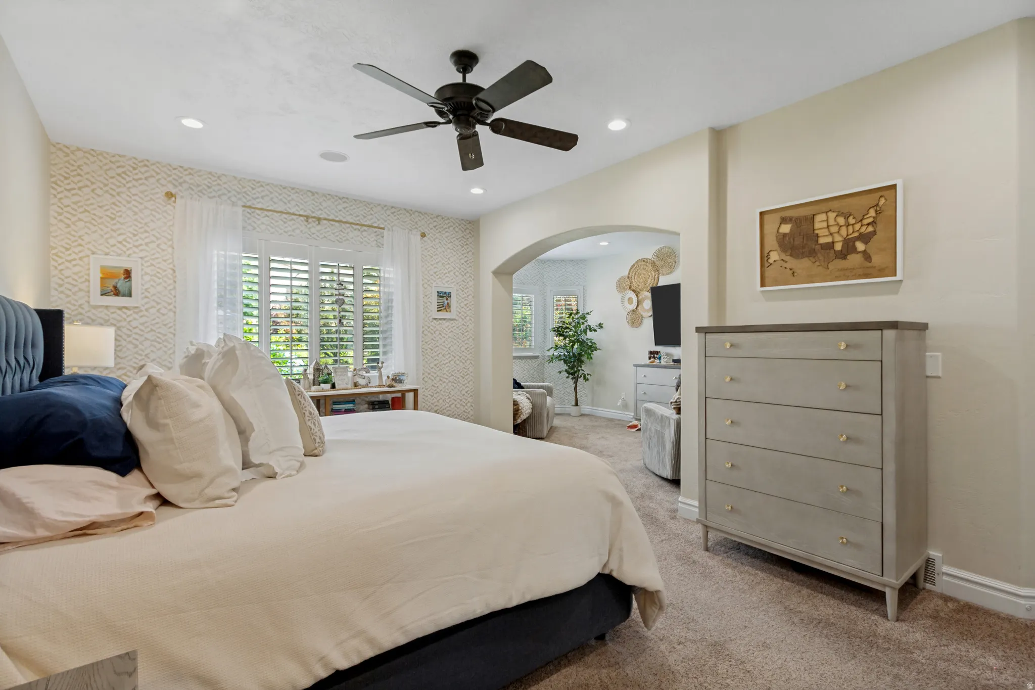 Recessed lighting, ceiling fan, accent wall with patterned wallpaper, plantation shutters, and an arched entryway