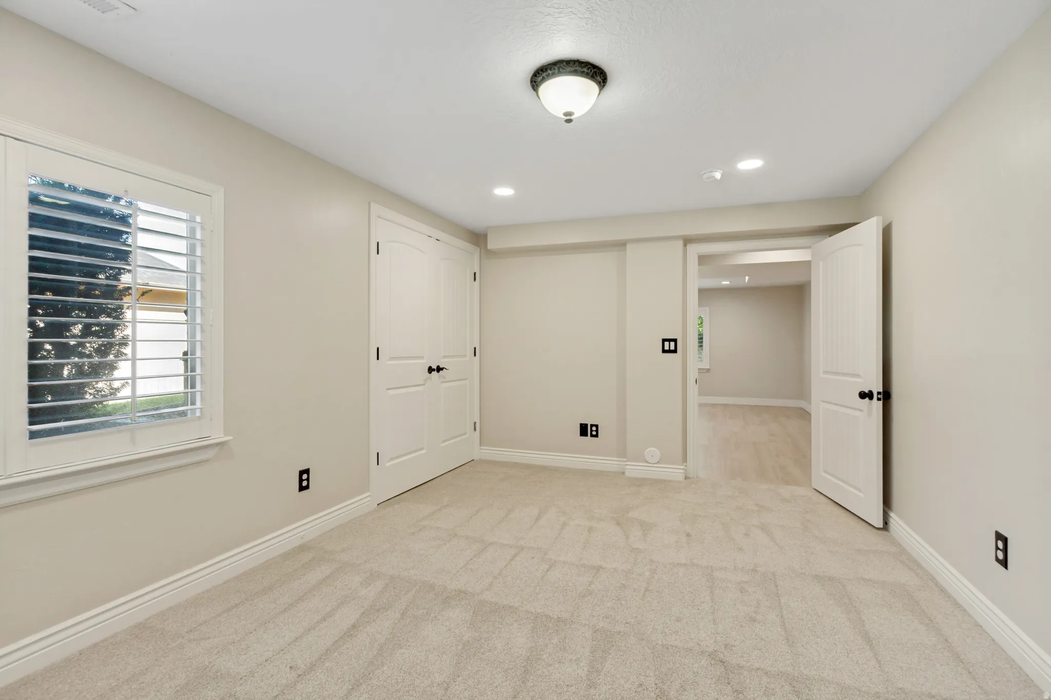 Light-colored carpeting, white plantation shutters, white paneled doors with black hardware, recessed lighting, and a flush-mount ceiling fixture