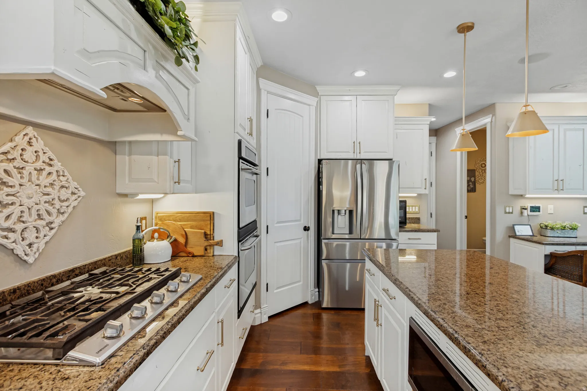 White cabinetry with brushed nickel hardware, stainless steel appliances, granite countertops, built-in double ovens, and wood-finish flooring