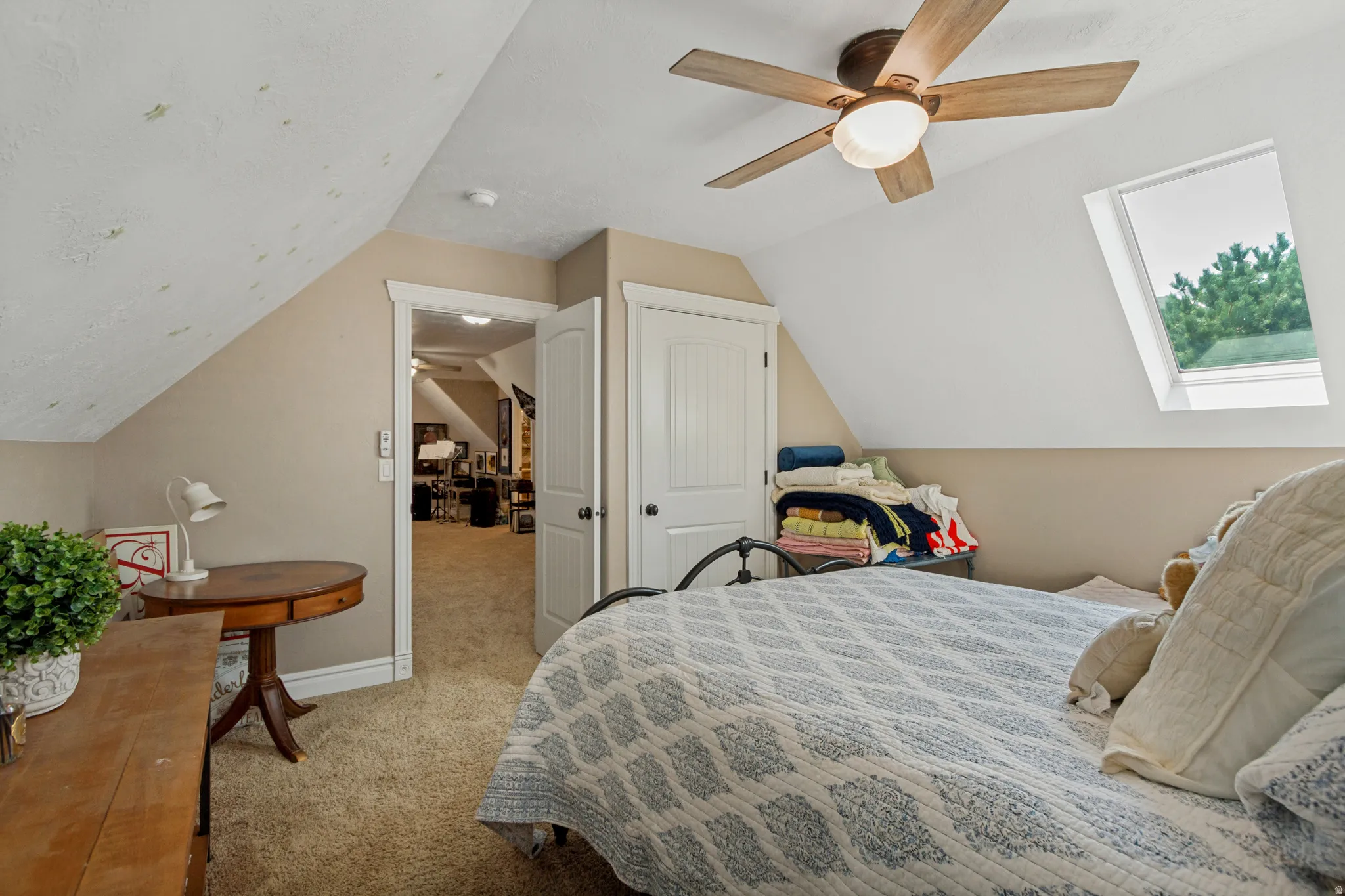 Vaulted ceiling with an integrated skylight, wood-finish ceiling fan, and carpeted flooring