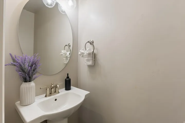 Pedestal sink with a brushed nickel faucet, large oval mirror, and wall-mounted light fixture