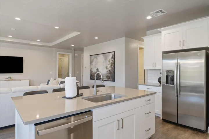 Open-concept kitchen featuring white cabinetry, stainless steel appliances, a large island with an undermount sink, and recessed lighting