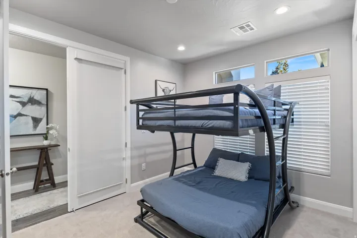 Recessed lighting illuminates this room featuring a metal bunk bed, carpet flooring, transom windows, and a white sliding door